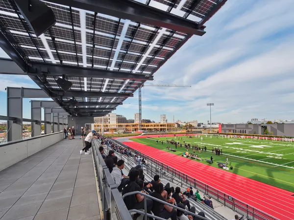 Fans on a covered rooftop terrace overlooking a stadium field